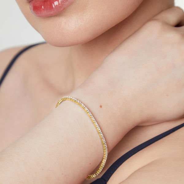 A yellow gold 2mm cubic zirconia tennis bracelet with cubic zirconia stones, featuring a snap fastening- JOOLS By Jenny Brown