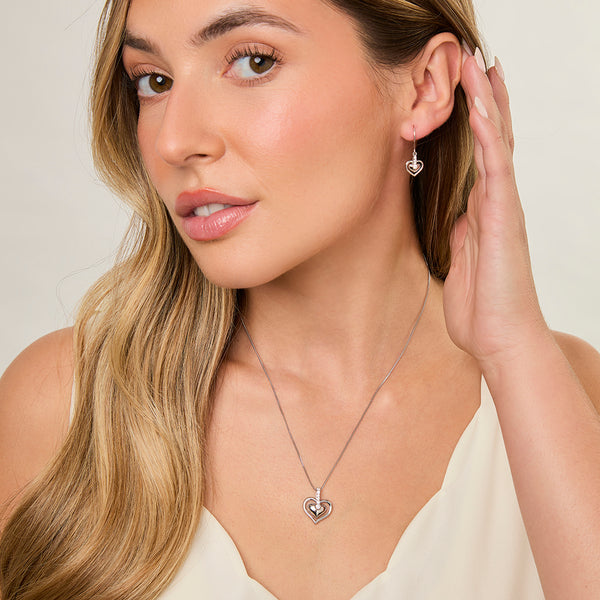 A pair of sterling silver heart-shaped drop earrings with a cubic zirconia in the center, dangle style.- JOOLS by Jenny Brown