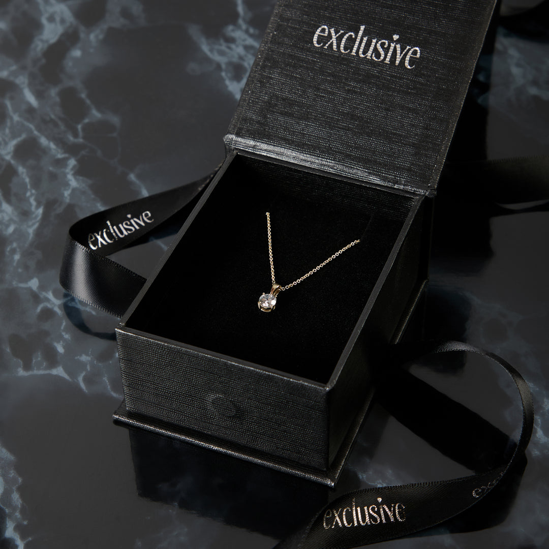 Gold necklace in an open black 'exclusive' box on a dark textured surface