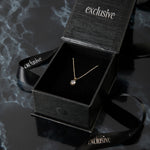 Load image into Gallery viewer, Gold necklace in an open black &#39;exclusive&#39; box on a dark textured surface
