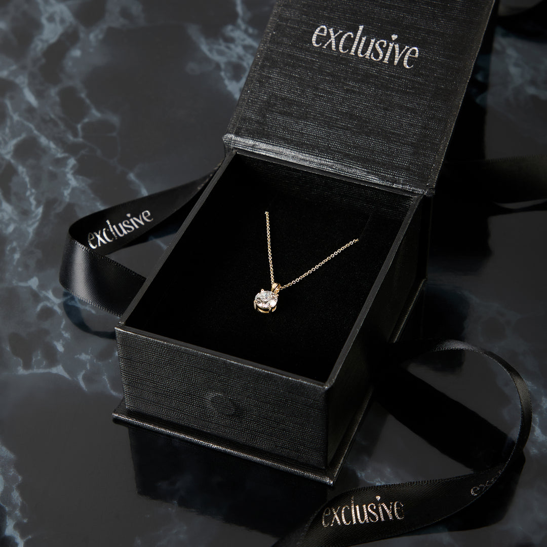 Gold necklace in an open black 'exclusive' box on a dark textured surface