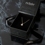 Load image into Gallery viewer, Gold necklace in an open black &#39;exclusive&#39; box on a dark textured surface
