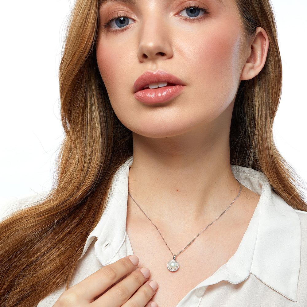 A sterling silver pendant with a central white freshwater pearl surrounded by a halo of cubic zirconia stones, on a silver chain-JOOLS by Jenny Brown