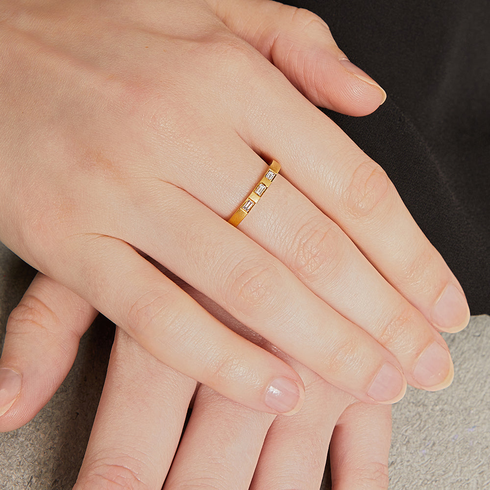 A yellow gold matte finish ring band with three baguette diamonds set on top.
