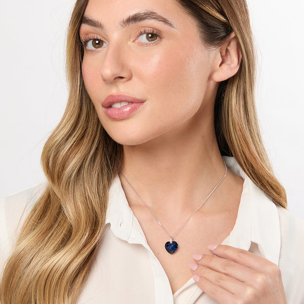 A sterling silver necklace with a large faceted heart-shaped sapphire blue cubic zirconia pendant, accompanied by smaller clear cubic zirconia accents at the top.