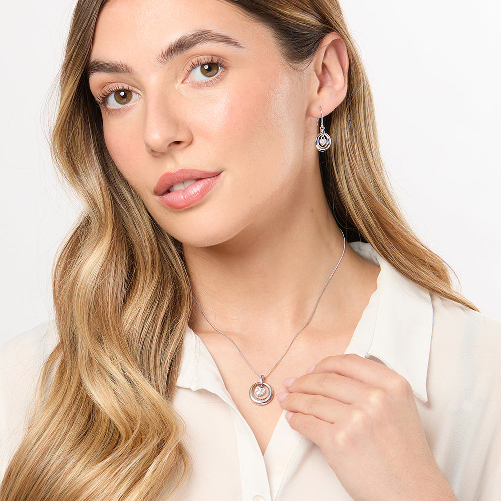 A pair of sterling silver hoop earrings with a heart-shaped cubic zirconia drop, one earring is shown from the front and the other from the back, both featuring a rhodium finish.