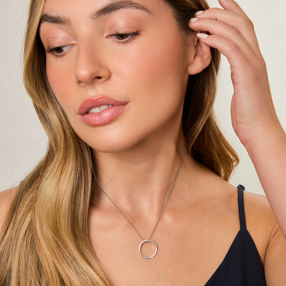 A sterling silver open circle pendant with cubic zirconia stones set in a semi-polished finish, attached to a silver chain.-JOOLS by Jenny Brown