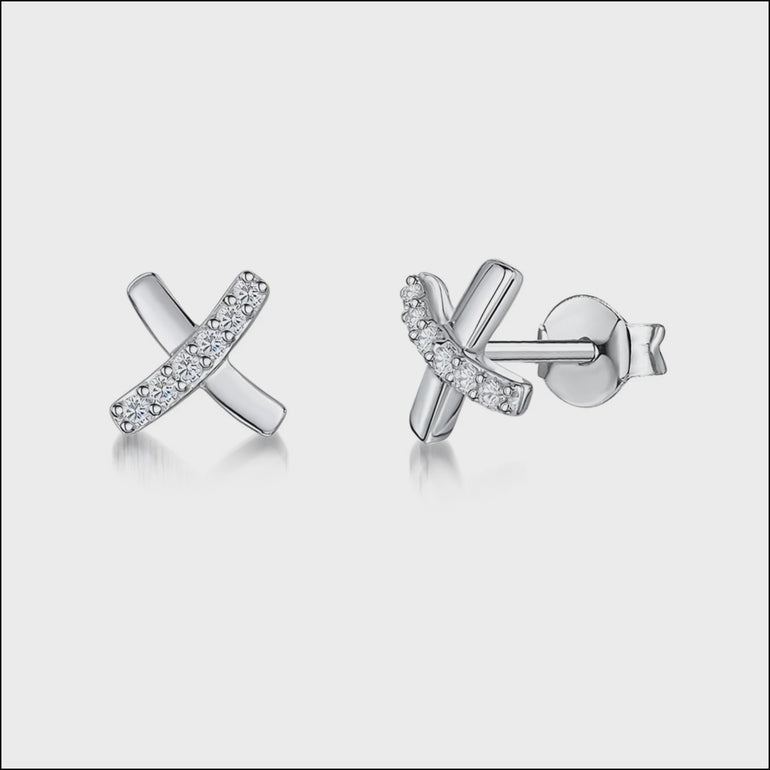 A pair of sterling silver stud earrings in a kiss or X-shape design, encrusted with cubic zirconia stones.- JOOLS By Jenny Brown