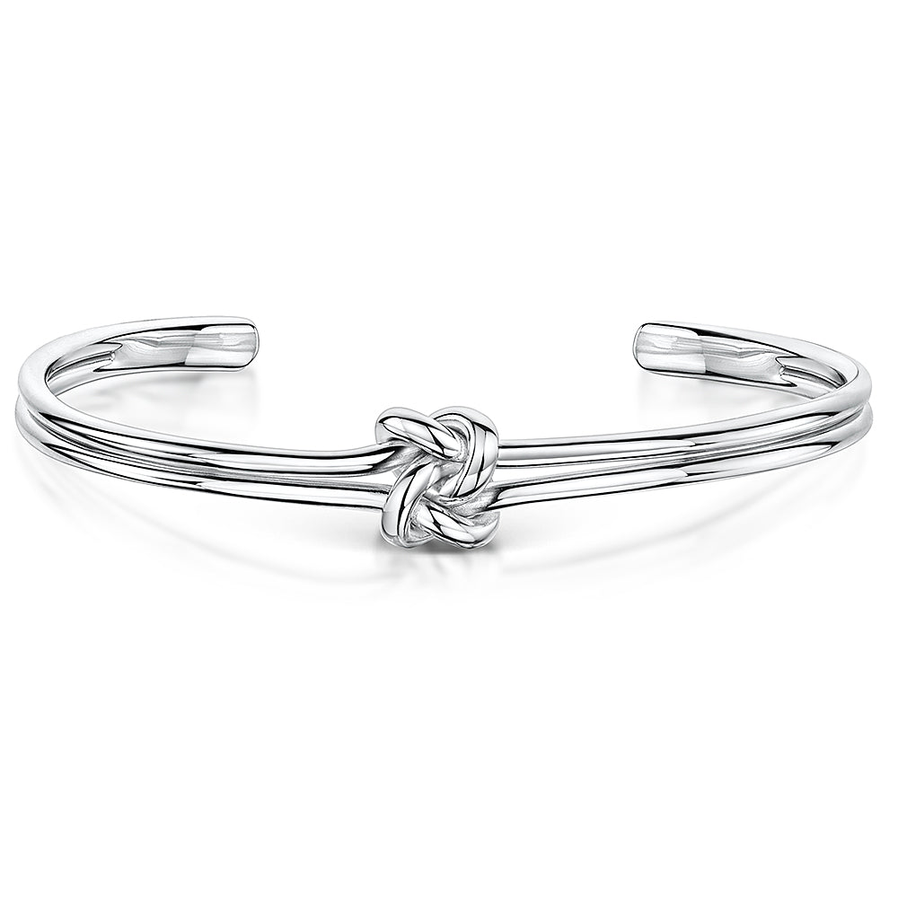 A polished silver-tone open cuff bracelet featuring a central love-knot motif. The band appears as two parallel rounded wires that loop into the knot at the center, tapering to smooth, rounded ends for an easy slip-on fit-JOOLS by Jenny Brown