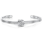 Load image into Gallery viewer, A polished silver-tone open cuff bracelet featuring a central love-knot motif. The band appears as two parallel rounded wires that loop into the knot at the center, tapering to smooth, rounded ends for an easy slip-on fit-JOOLS by Jenny Brown
